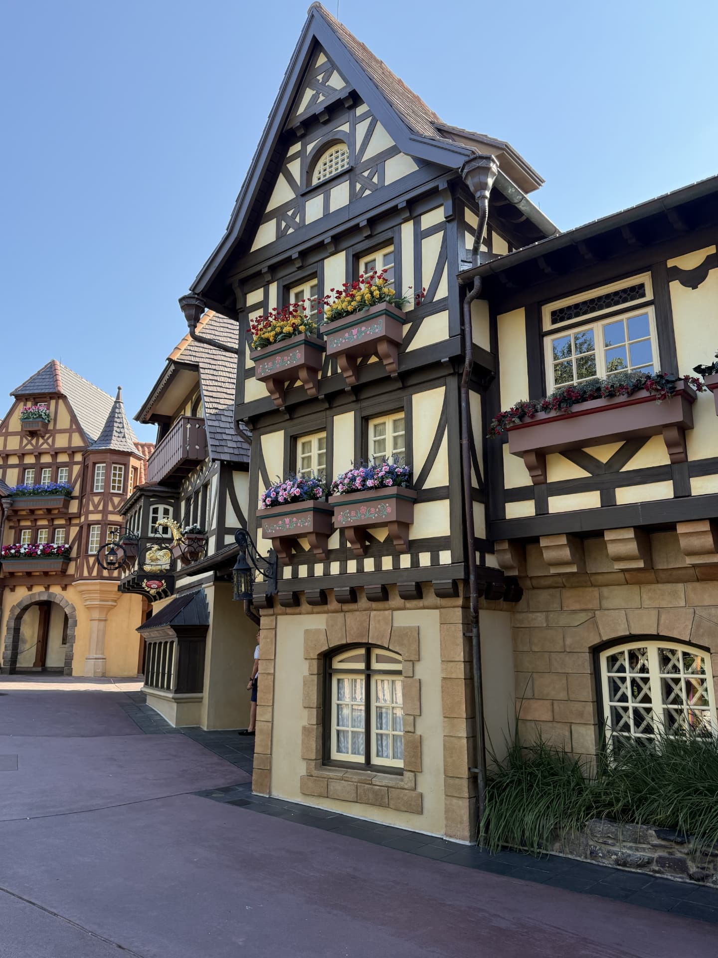 Flower-lined European-style pavilion at EPCOT under a clear blue sky.