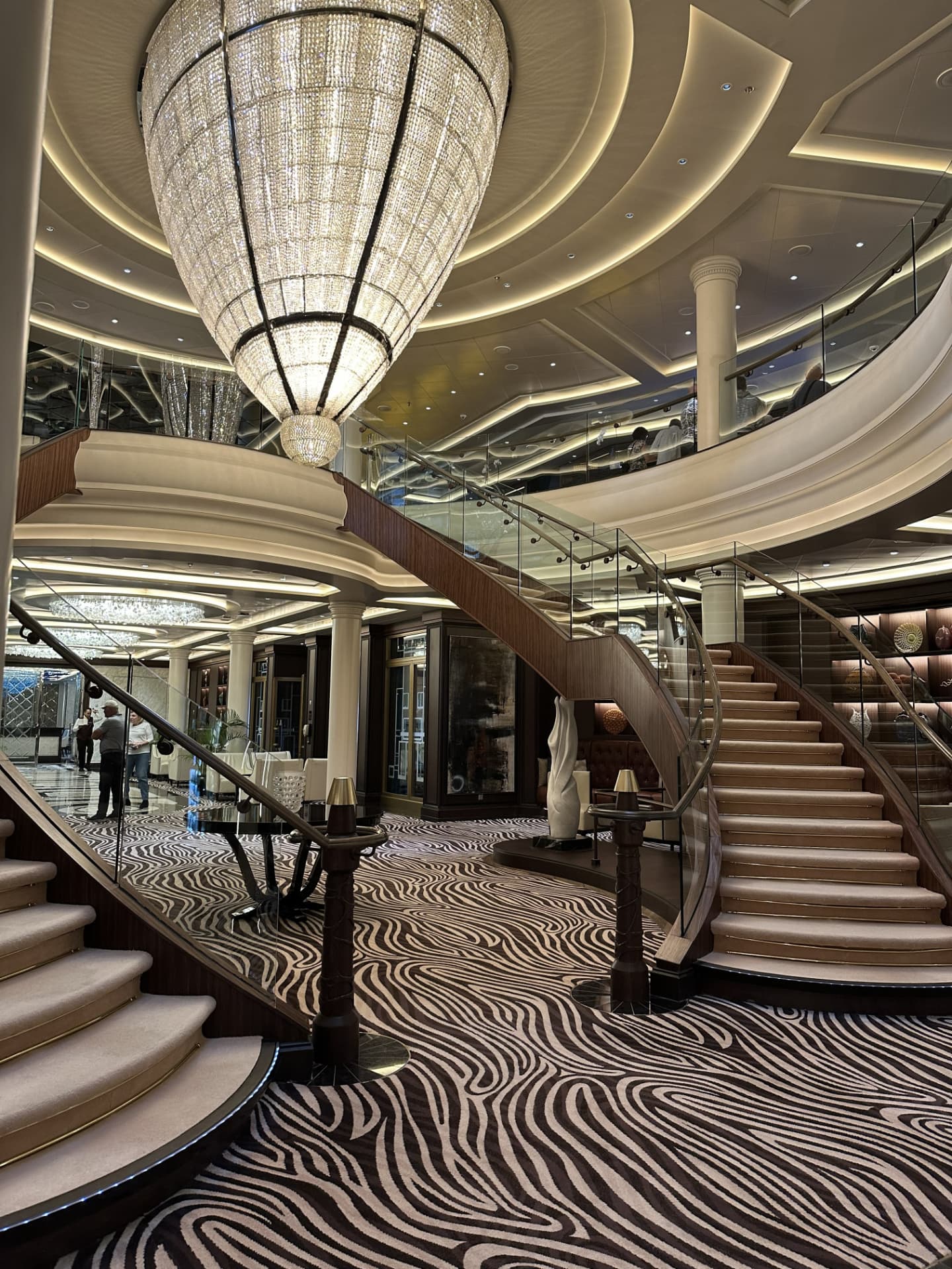 Luxury cruise ship atrium with a crystal chandelier and curved staircase with glass railings