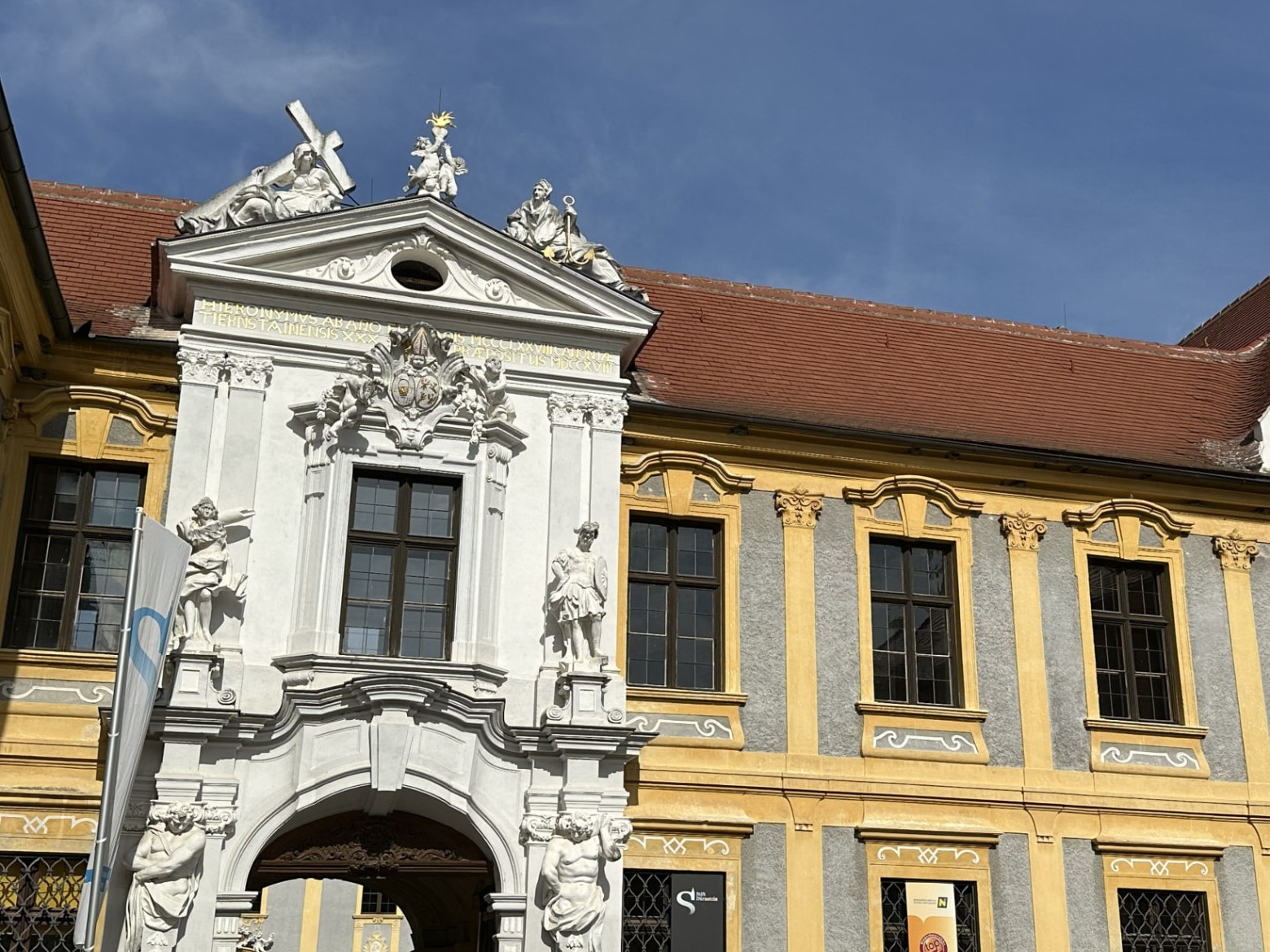 Baroque abbey gateway with white statues and a golden yellow facade under a blue sky in Dürnstein, Austria