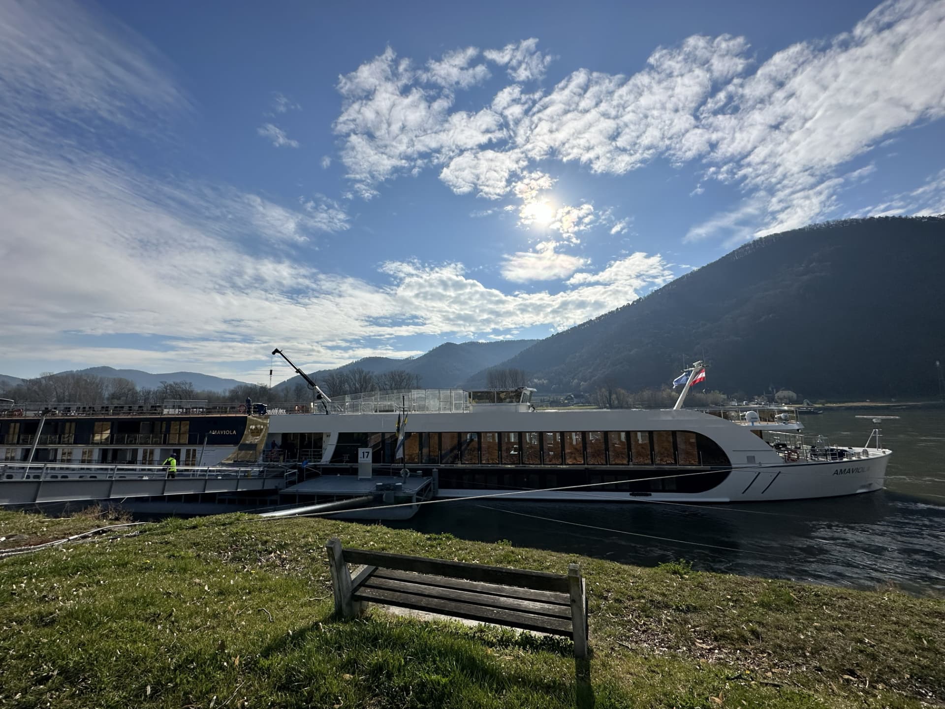 AmaWaterways river cruise ship docked along the Danube below forested hills on a sunny day