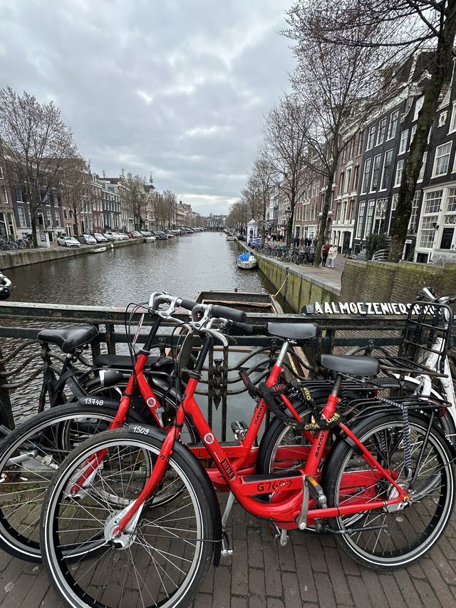 Red Dutch bicycles parked on a bridge railing above an Amsterdam canal lined with gabled houses