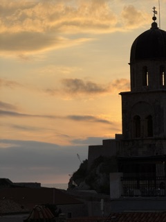 Bell tower silhouetted against a golden Dubrovnik sunset